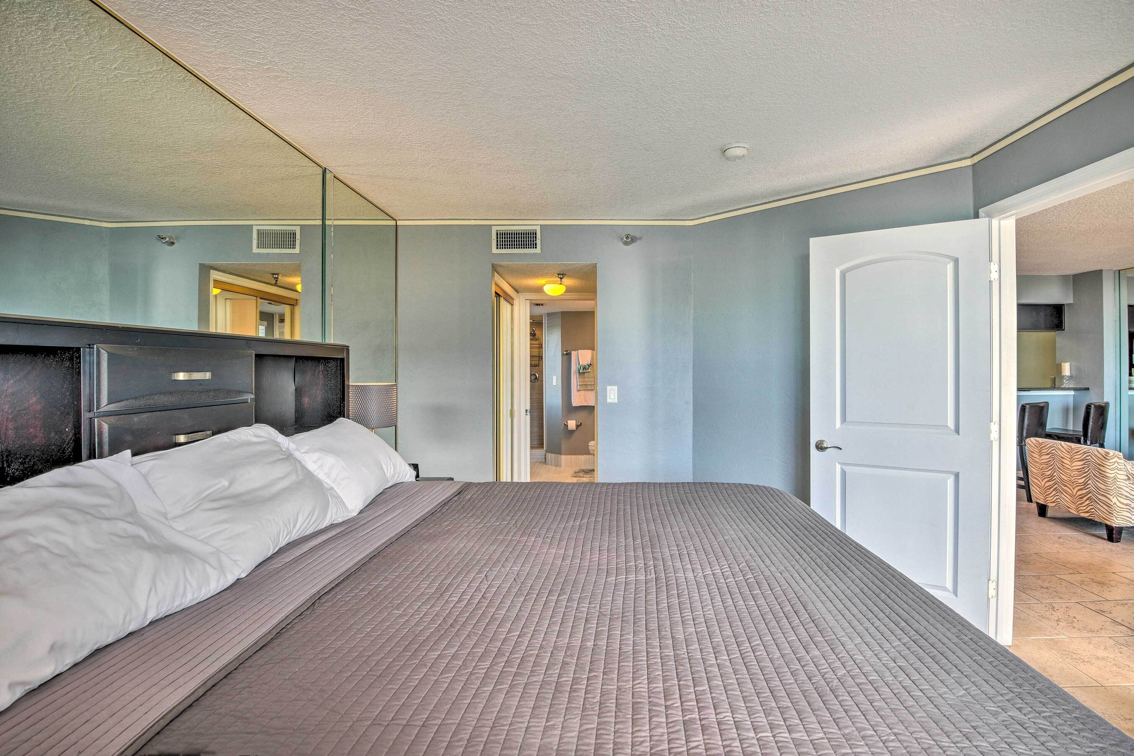 A bedroom with a large bed, a mirror, and a door leading to a bathroom.