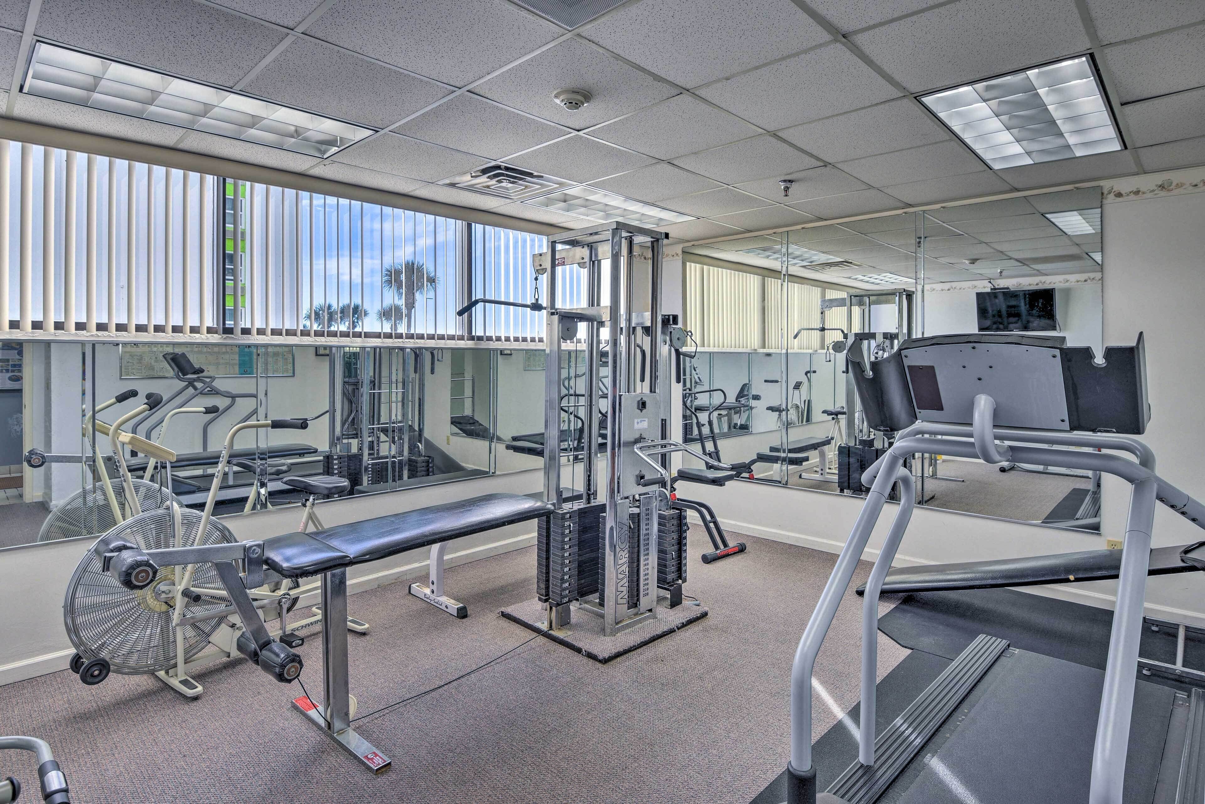 Ein Fitnessstudio mit verschiedenen Trainingsgeräten, großen Fenstern und einer Spiegelwand.