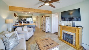 A living room with a fireplace, a television, a ceiling fan, and a kitchen in the background. - Unwind Fireside: Ozark Mtn Condo w/ Resort Perks! (Branson West)