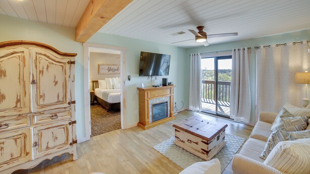 A living room with a fireplace, a television, a sofa, and a view to the outside. - Unwind Fireside: Ozark Mtn Condo w/ Resort Perks! (Branson West)