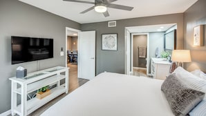 A modern bedroom with a large bed, a ceiling fan, a TV, and a bathroom visible through an open door.