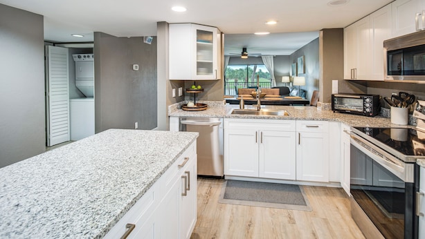 A modern kitchen with granite countertops, white cabinets, a built-in oven, and a microwave.