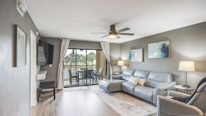 A modern living room with a grey sofa, a ceiling fan, and a view to an outdoor patio.