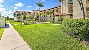 A multi-story hotel with a courtyard featuring well-maintained grass and palm trees.