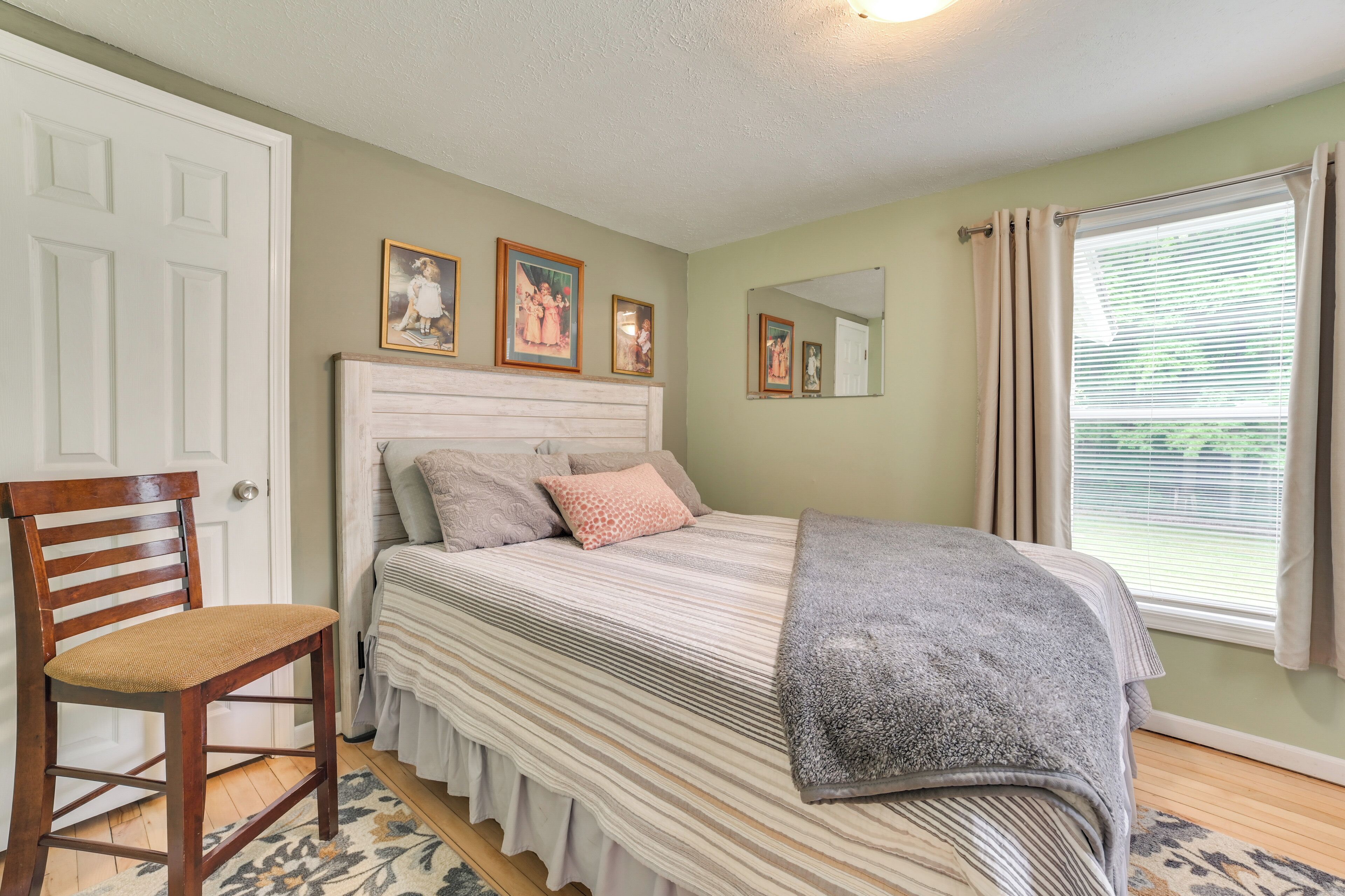 A bedroom with a bed, a chair, a mirror, and a window with curtains.