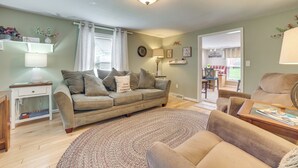 A cozy living room with a sofa, a coffee table, and a lamp. There is a window with curtains and a door leading to another room. - Visit Fife Lake & Traverse Bay! Farmhouse Hideaway (Fife Lake)
