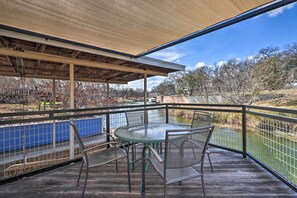Un espace extérieur abrité, doté d’une table et de chaises, qui offre une vue sur un plan d’eau et un parc.