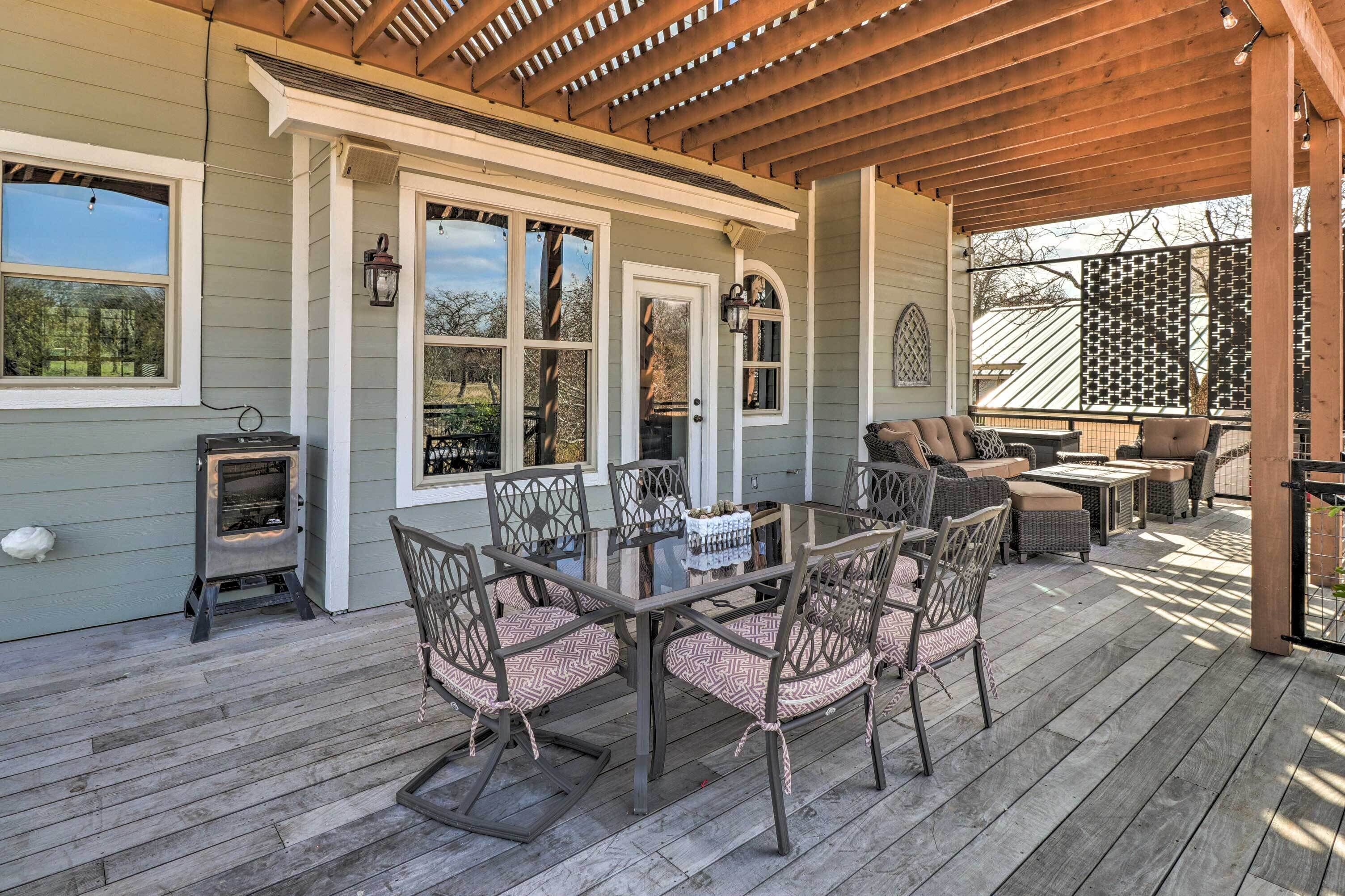 A covered patio with a wooden table and chairs, a built-in wood stove, and a seating area with a sofa and ottoman.
