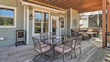 A covered patio with a wooden table and chairs, a built-in wood stove, and a seating area with a sofa and ottoman.