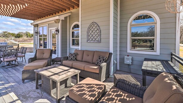 An outdoor patio with wicker furniture, a covered seating area, and a view of the surrounding landscape. - Lake LBJ Waterfront Vacation Rental! (Marble Falls)