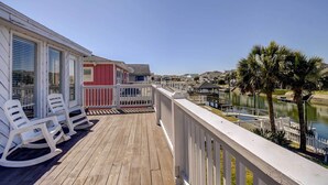 A wooden deck with rocking chairs, a white railing, and a view of a lake and houses. - Ocean Isle Beach Home w/ Canal Views! (Ocean Isle Beach)