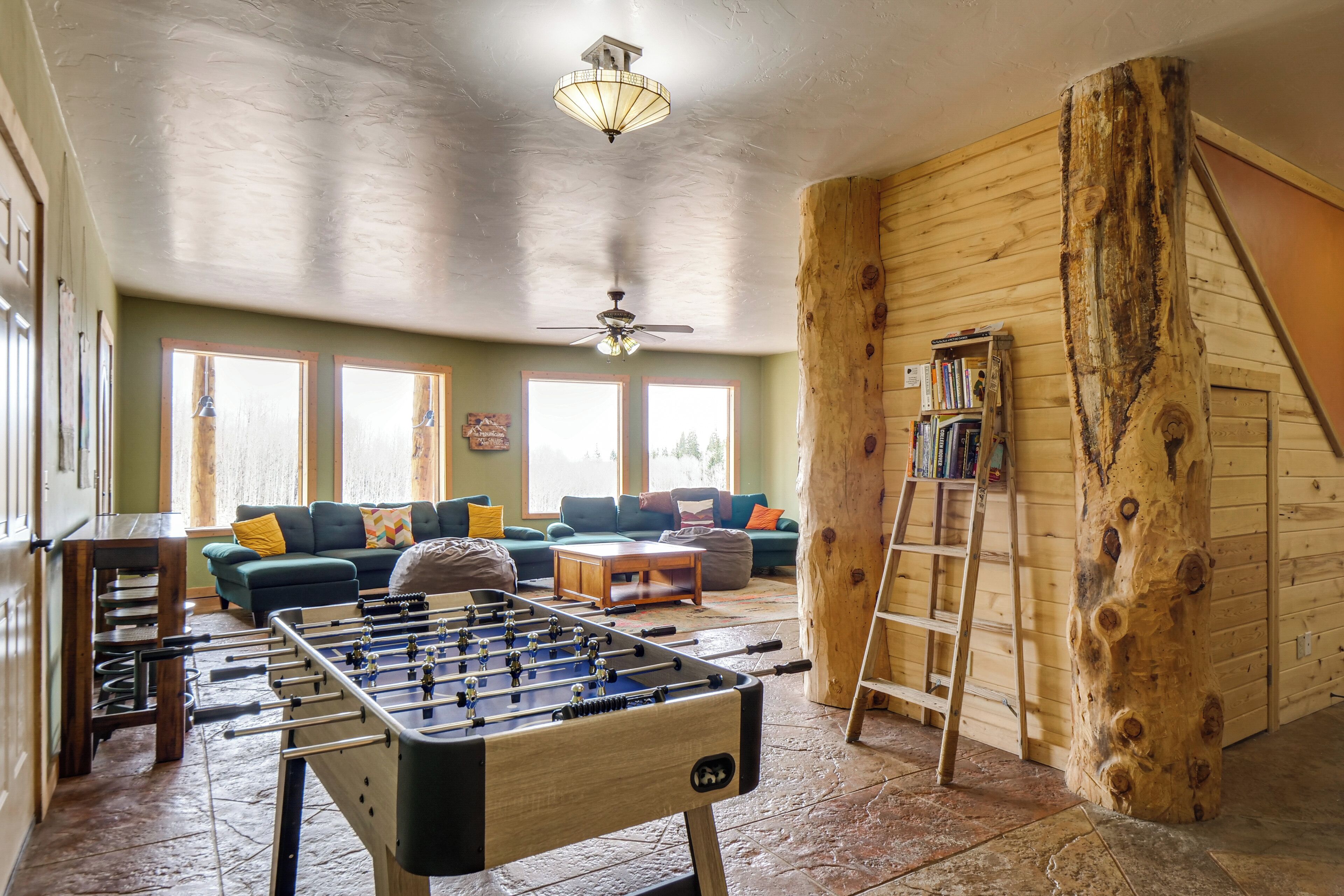 A cozy living room with a foosball table, sofas, a coffee table, and a ladder against a wooden wall.