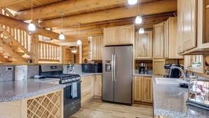 A wooden cabin interior with a kitchen featuring a stainless steel refrigerator, granite countertops, and wooden cabinetry. - 5 Acres of Scenic Beauty! Large Fairplay Log Home (Fairplay)