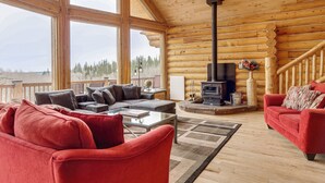 A log cabin interior with a fireplace, red sofas, a glass coffee table, and large windows offering a view of the forest. - 5 Acres of Scenic Beauty! Large Fairplay Log Home (Fairplay)