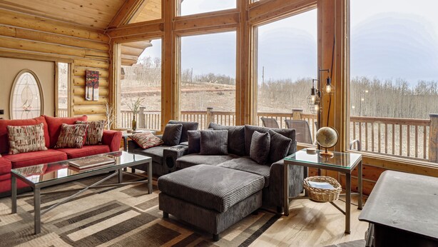 A log cabin interior with a large window, a red sofa, a gray sectional, and a glass coffee table. - 5 Acres of Scenic Beauty! Large Fairplay Log Home (Fairplay)