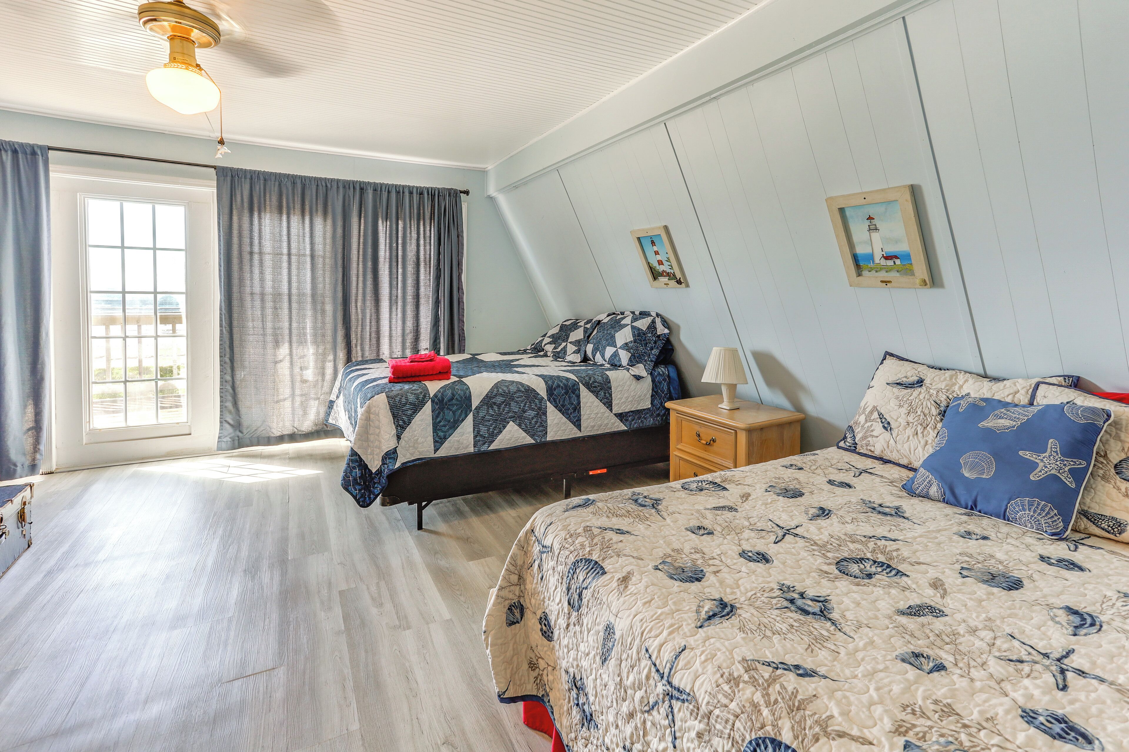 Un dormitorio con dos camas, un ventanal grande y un ventilador de techo.