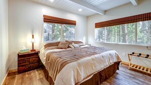 A bedroom with a large bed, wooden nightstand, and a window with a view of trees.