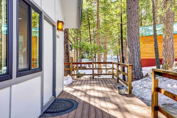 A wooden deck with a metal railing, surrounded by trees and a red building in the background.