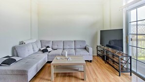 Ein modernes Wohnzimmer mit einem grauen Ecksofa, einem Holztisch und einem Fernseher auf einem Schrank.