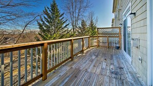 Eine Holzterrasse mit Geländer, ein Gebäude mit einem Fenster und Bäume im Hintergrund.