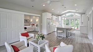 A spacious living area with a kitchen and dining area, featuring white cabinetry, a ceiling fan, and a large window providing natural light. - Contemporary Tacoma Cottage w/ Deck & Pond! (Tacoma)