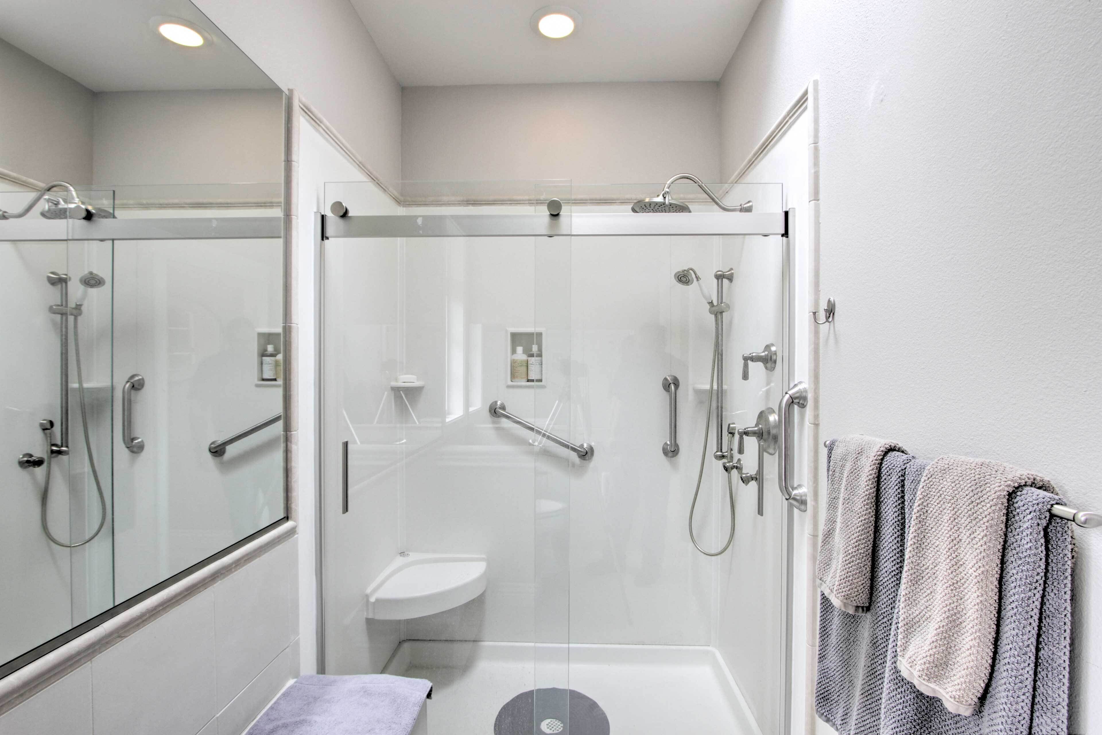 Un baño moderno con ducha acristalada, un lavamanos pequeño y un perchero para toallas.