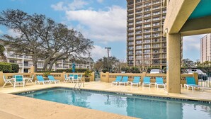 A swimming pool with lounge chairs, a tall building in the background, and a clear sky. - Condo w/ Ocean View + Pool Access! (Myrtle Beach)