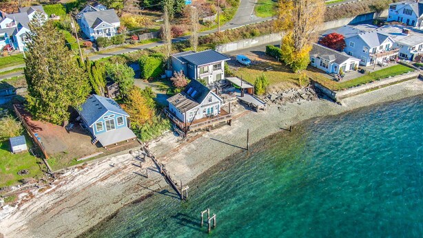 Vue aérienne d’une zone résidentielle côtière, avec des maisons, une côte bien définie et un quai.