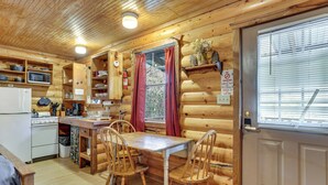 A wooden cabin interior with a kitchen, dining table, chairs, a microwave, and a refrigerator. - Cedar Falls Cabin: Nestled by Honey Creek (Davis)