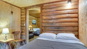 A log cabin-style room with a bed, a chair, a nightstand, and a lamp. - Cedar Falls Cabin: Nestled by Honey Creek (Davis)
