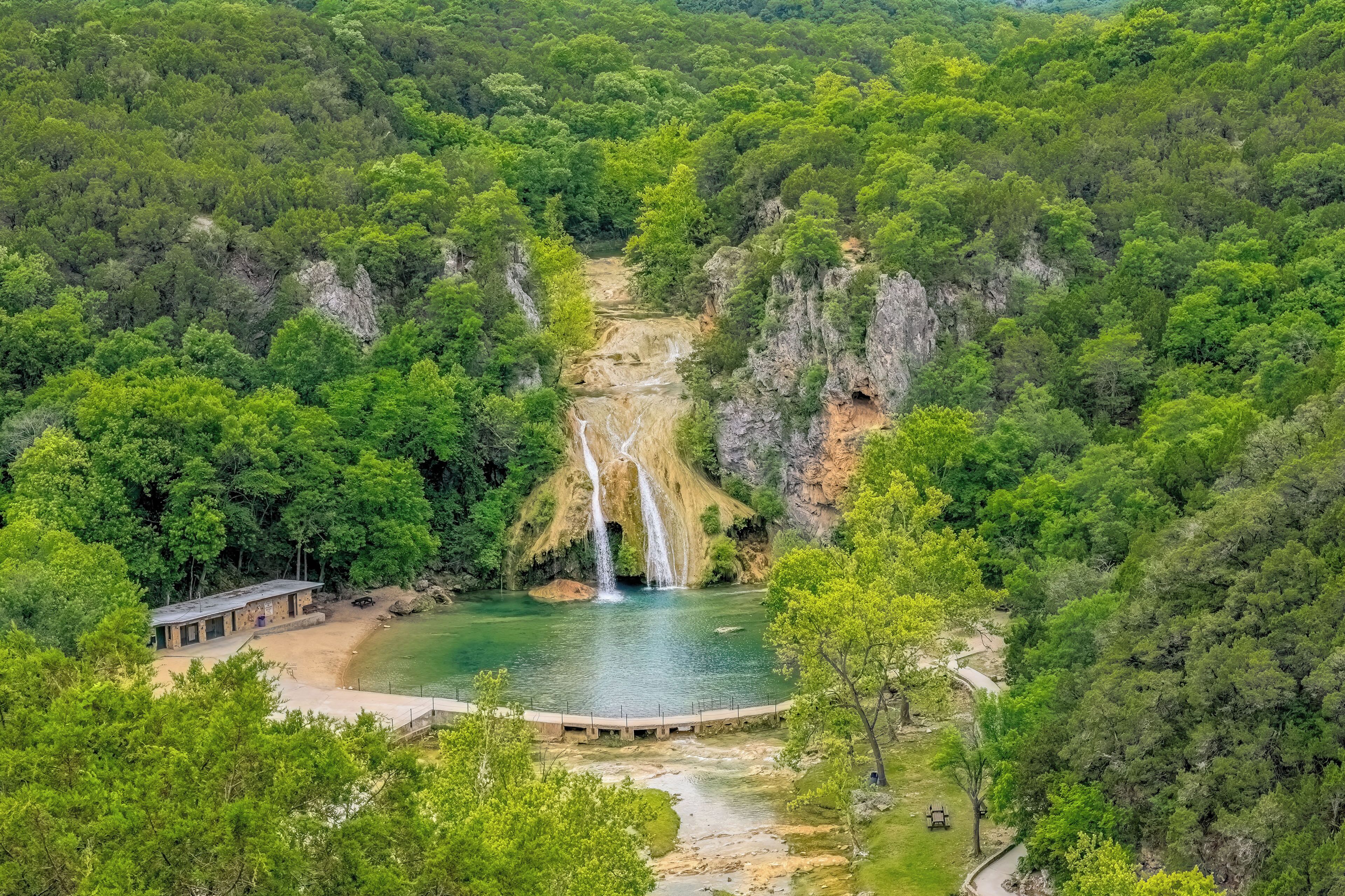 Un paisaje natural con una cascada, un edificio pequeño y un puente sobre un río.