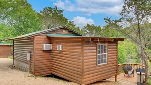 A wooden cabin with a porch, a window, and a door. - Cedar Falls Cabin: Nestled by Honey Creek (Davis)