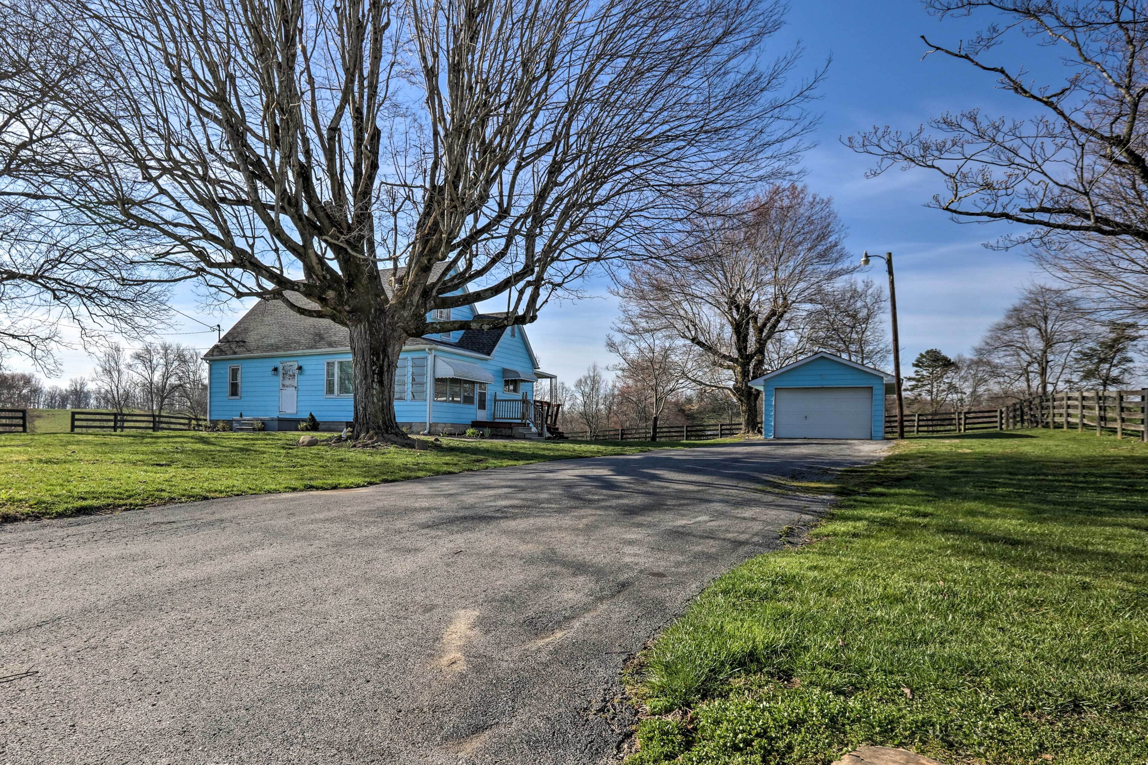Una casa azul con un gran árbol en el frente, un camino de entrada y un pequeño garaje.