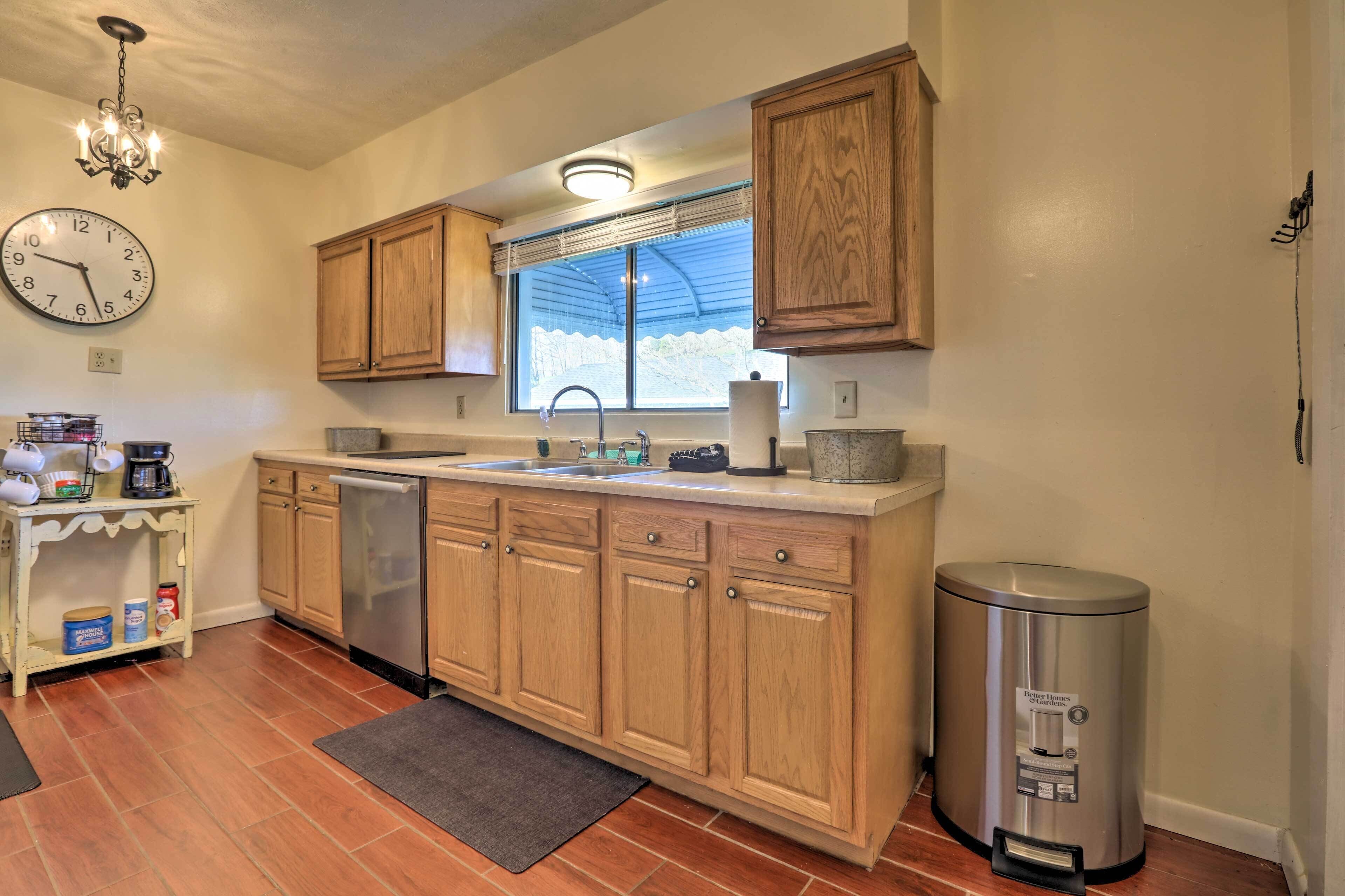 A kitchen with wooden cabinets, a stainless steel dishwasher, a sink, a clock, and a trash can.