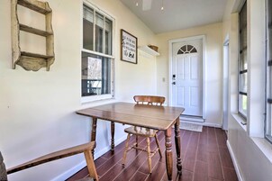 Un comedor con mesa y sillas de madera, una ventana con persianas, una puerta y un estante de pared con un objeto decorativo.