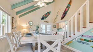A dining area with a white table and chairs, a ceiling fan, and surfboards on the wall. - Cape Canaveral Cottage w/ Pool - Walk to Beach! (Cape Canaveral)