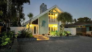 A two-story house with a stone chimney, a balcony, and a well-lit entrance. - Cape Canaveral Cottage w/ Pool - Walk to Beach! (Cape Canaveral)