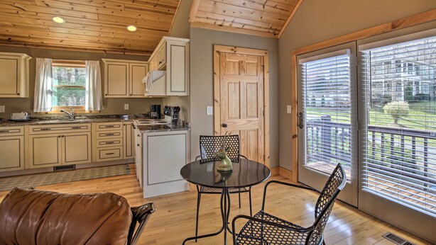 Una cocina con armarios de madera, una mesa de comedor con sillas y vistas a un jardín trasero a través de ventanas amplias.