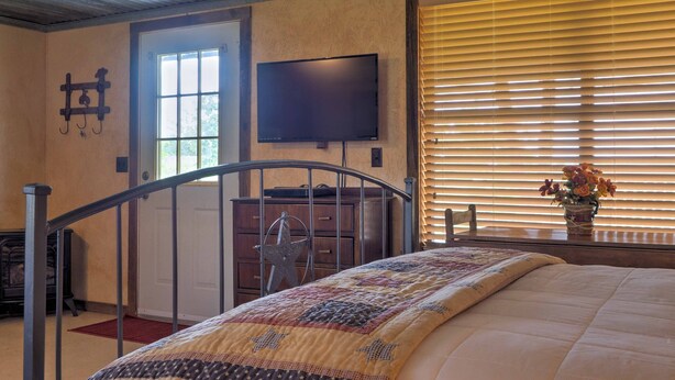 A bedroom with a bed, a television, a dresser, and a window with blinds.
