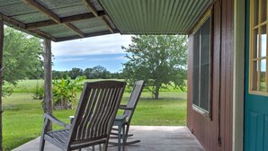 A porch with two rocking chairs, a wooden door, and a view of a green field.