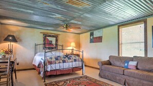 A bedroom with a metal bed frame, a wooden desk, a brown sofa, a patterned rug, and a Texas flag on the wall.
