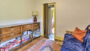 A room with a wooden dresser, a lamp, a patterned rug, and a blue sofa with an orange pillow. - Pet-friendly Roxbury Farmhouse on 350 Acres! (Roxbury)
