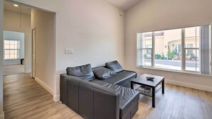 Una sala de estar moderna con un sofá de cuero negro, una mesita de centro pequeña y un amplio ventanal con vista a la calle.