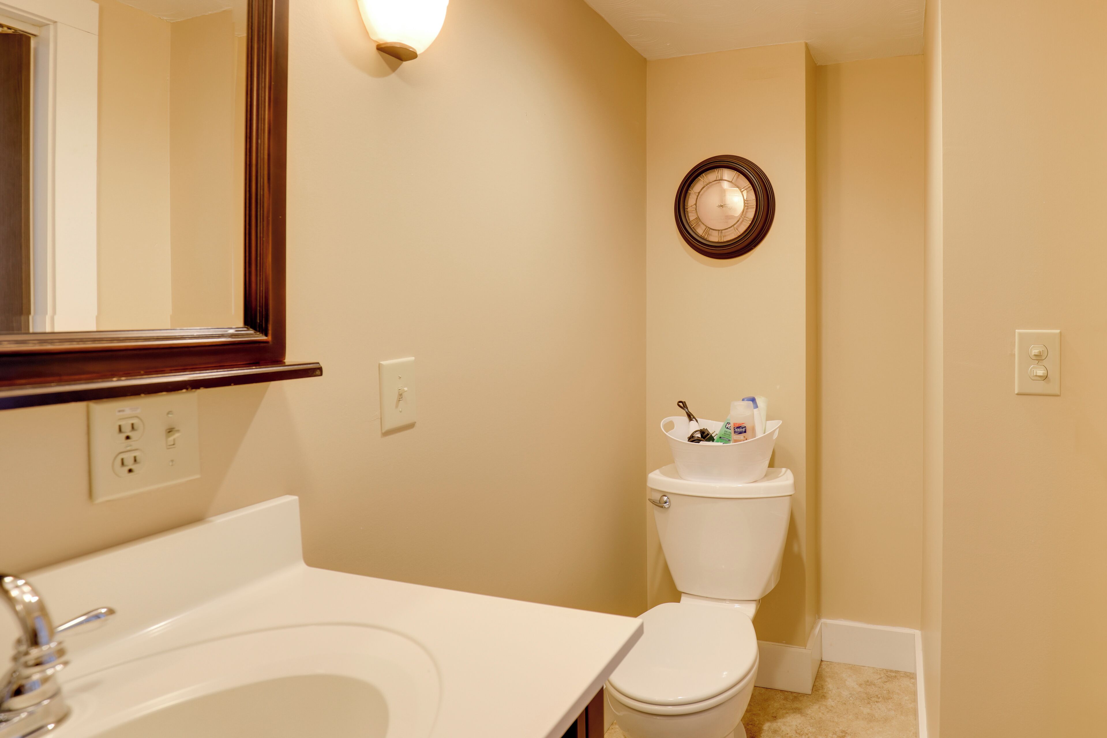 A bathroom with a white sink, a mirror, a toilet, and a wall-mounted clock.