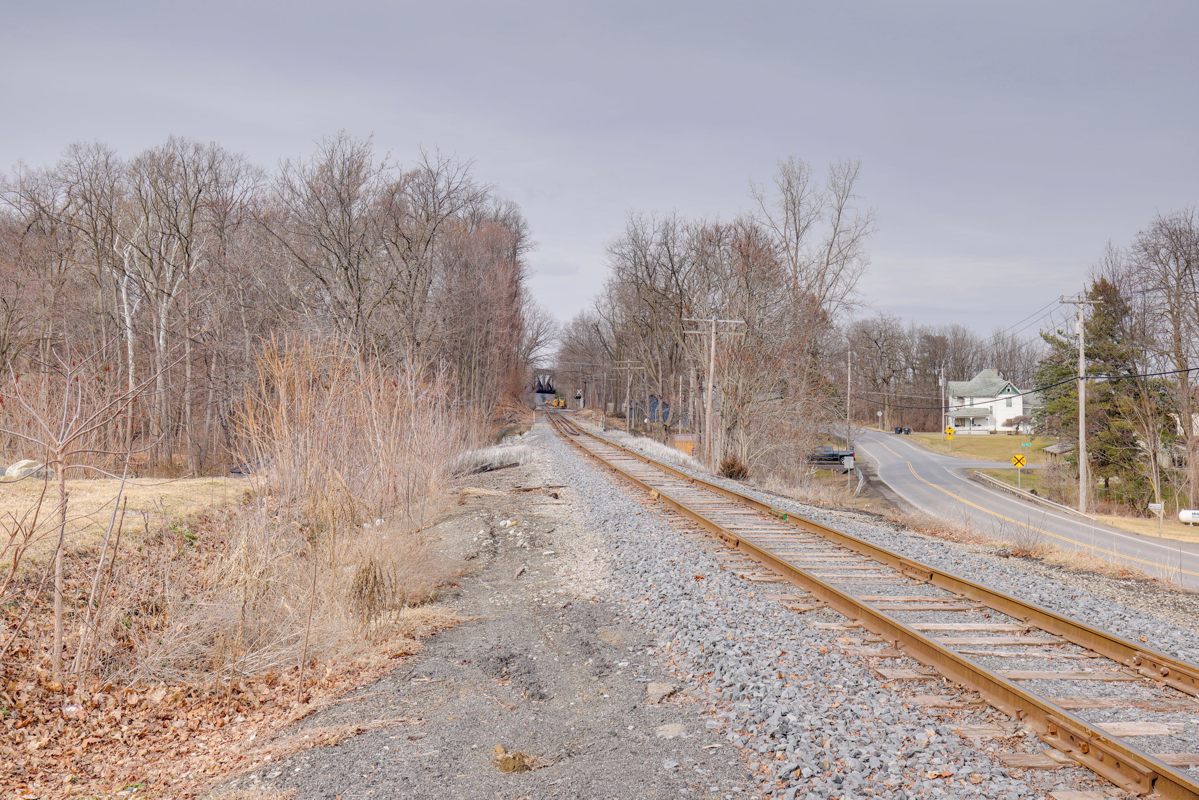 A railway track with a road on the right, surrounded by leafless trees and a distant building.