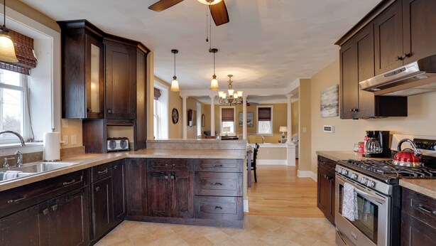 A spacious kitchen with dark wood cabinets, a central island, a stove, and a ceiling fan. - Finger Lakes Retreat: 3 Mi to Seneca & Keuka Lake (Himrod)