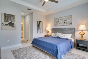 Une chambre à coucher avec un grand lit, deux tables de chevet avec des lampes, un ventilateur de plafond et des œuvres d’art accrochées aux murs.