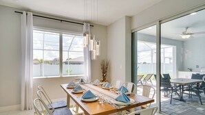 A dining area with a long table set for six, white chairs, and a view of the outdoor patio.
