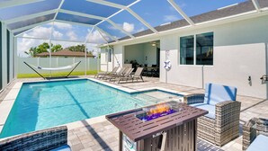 A pool area with a glass enclosure, lounge chairs, and a fire feature.