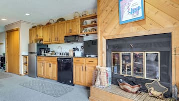 A kitchen with wooden cabinets, a black refrigerator, a microwave, and a fireplace with decorative items.